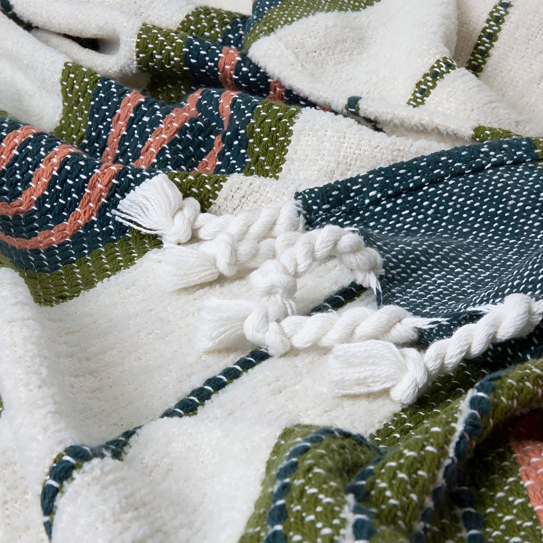 Close-up of the woven texture and tassel detail of the Zephyr throw blanket in green hues.